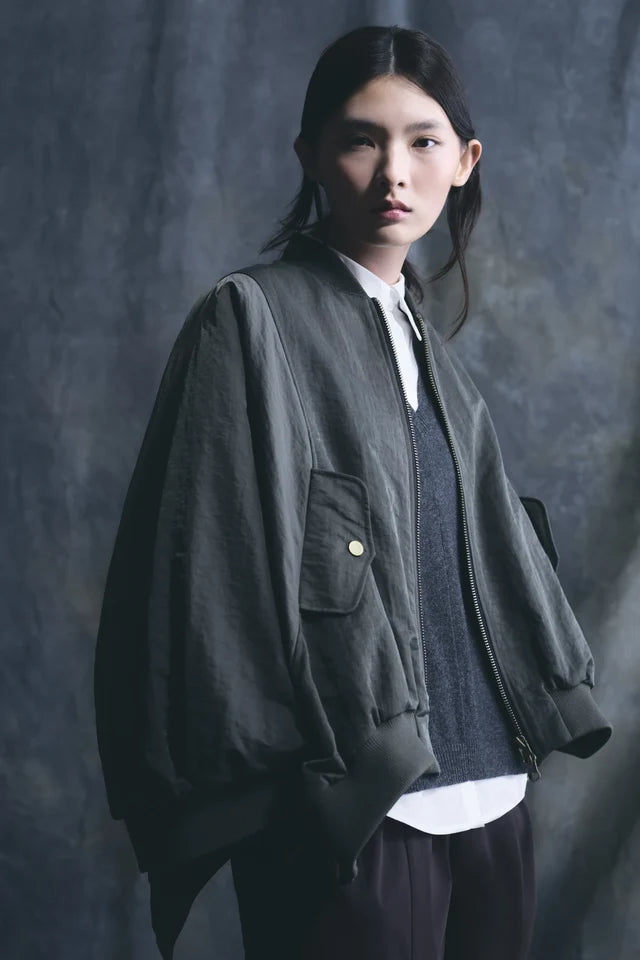 Person wearing a gray jacket over a white shirt with a dark background