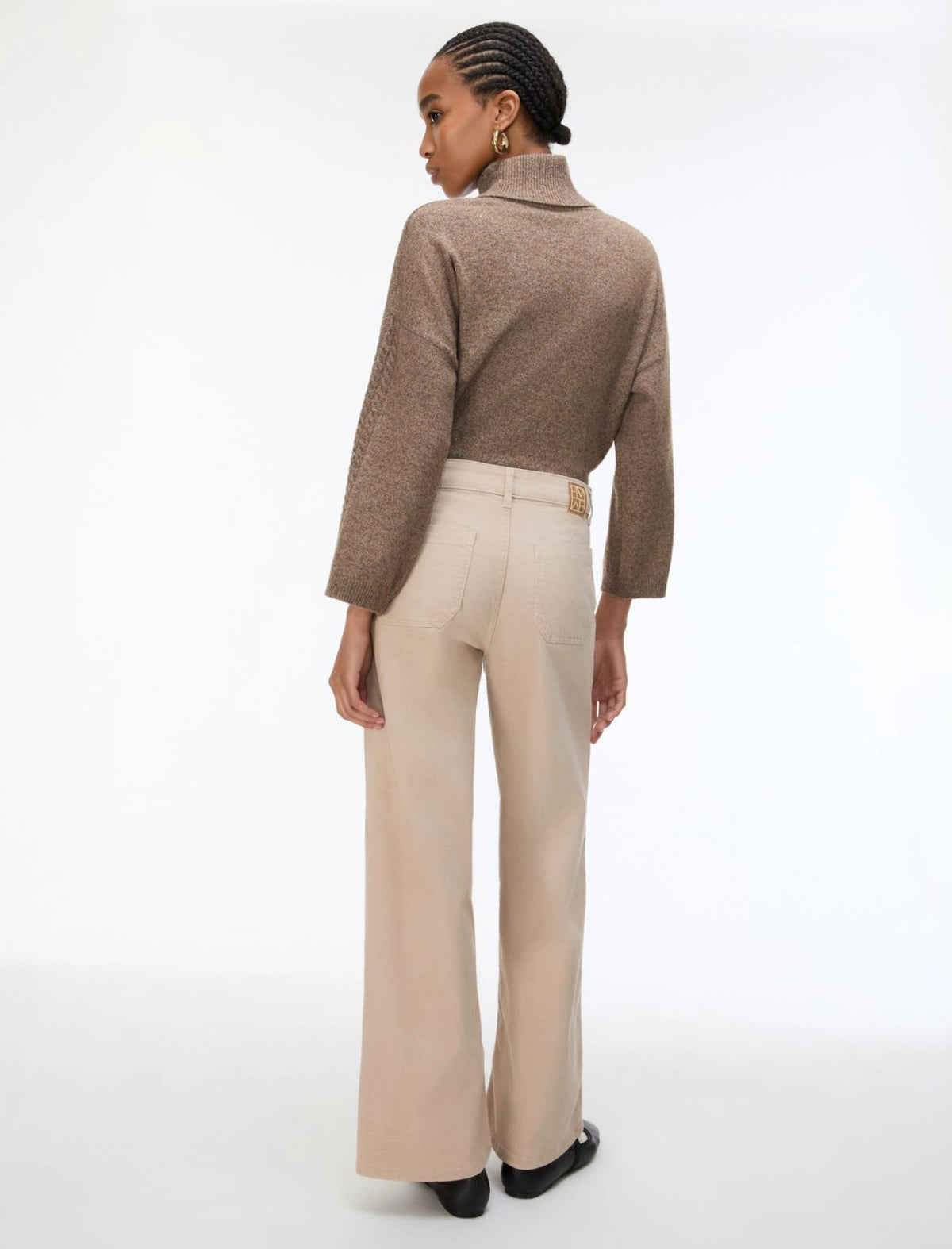 A model shown from the back wearing a textured taupe-brown mock-neck sweater and high-waisted beige wide-leg trousers, set against a plain white studio background.