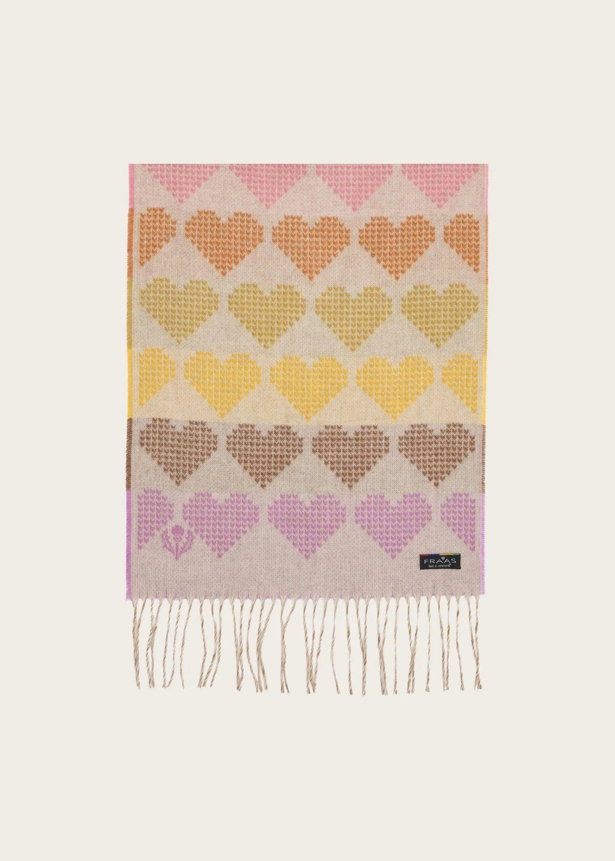 A rectangular woven scarf with fringe, featuring a repeating heart pattern in pink, orange, yellow, brown, and purple on a light beige background. A small black label with white text is visible near the bottom right corner.